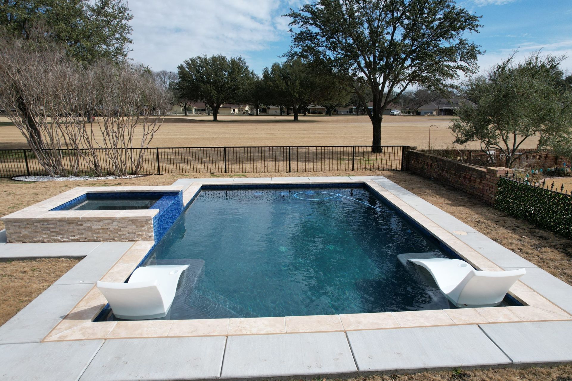 Backyard swimming pool with white coping and a grassy field beyond