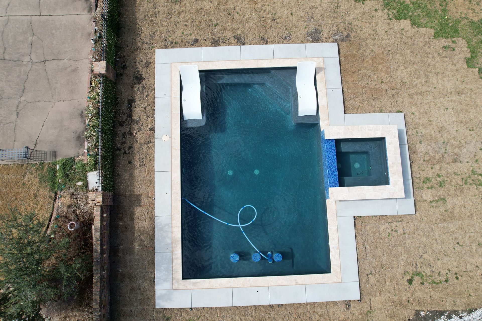 Aerial view of a backyard swimming pool with a cleaning hose and attached spa area
