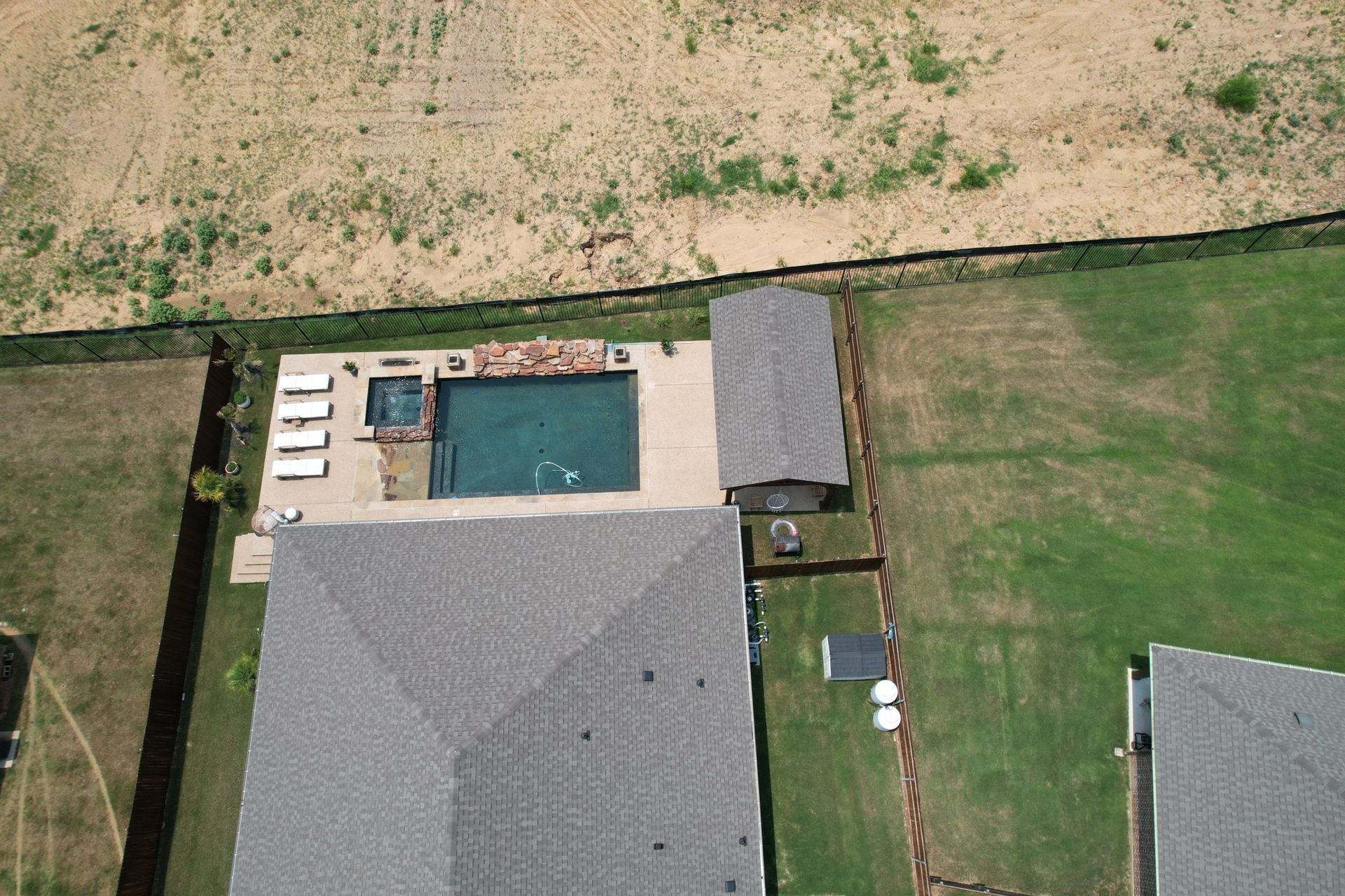 Aerial view of a house with a backyard pool, patio chairs, and a large green lawn.