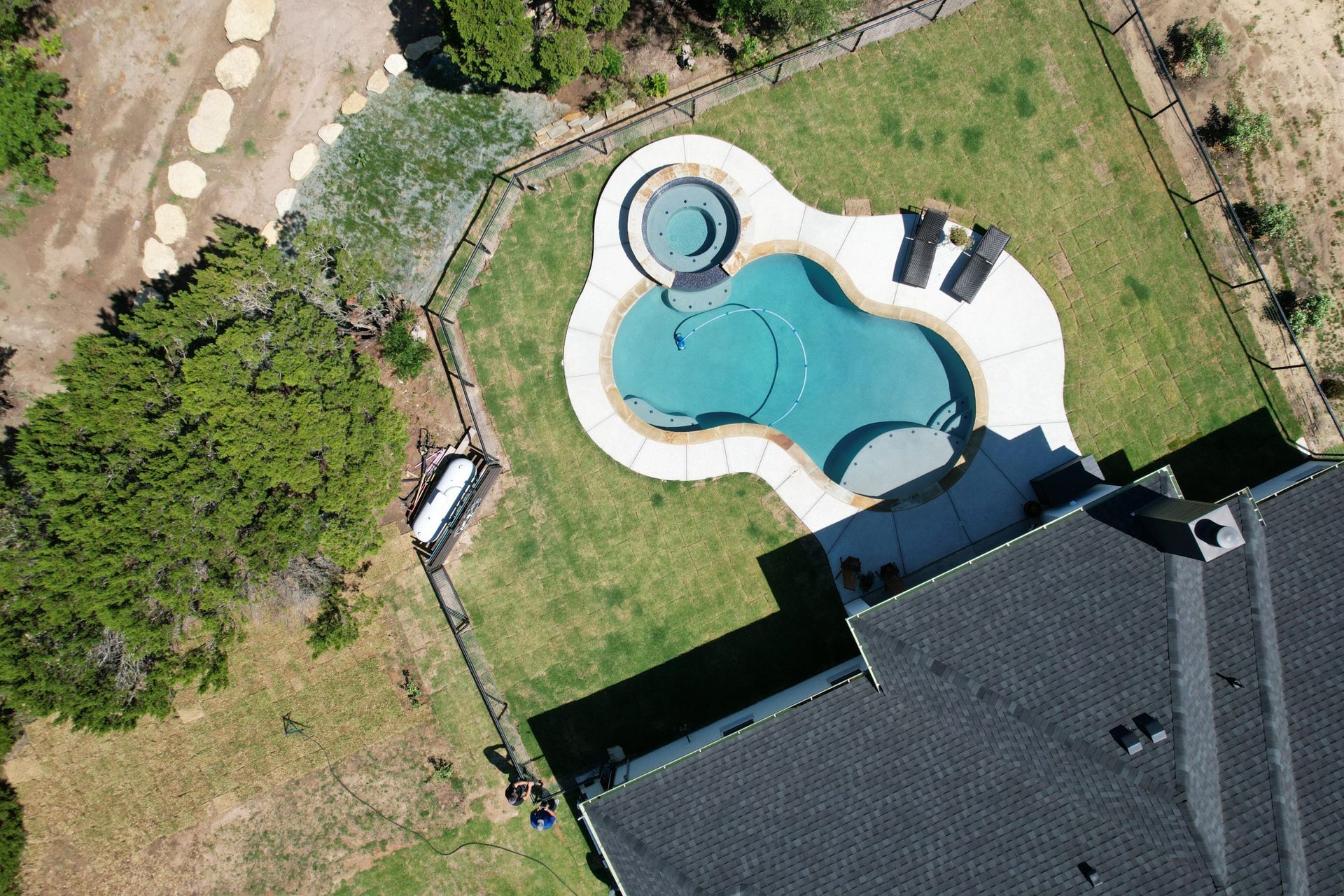 Aerial view of a backyard with a kidney-shaped pool, hot tub, lawn, and part of a house.