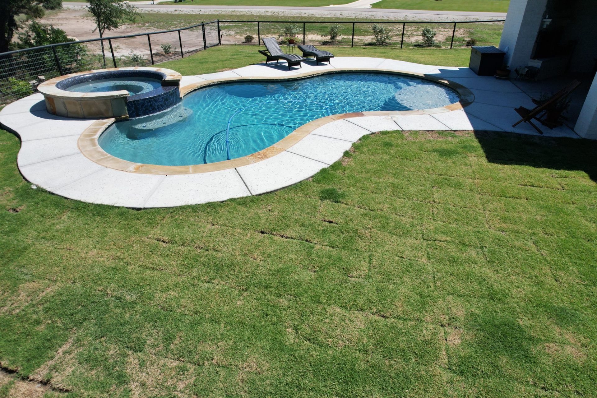 Backyard swimming pool with attached hot tub, surrounded by grass and a patio area.
