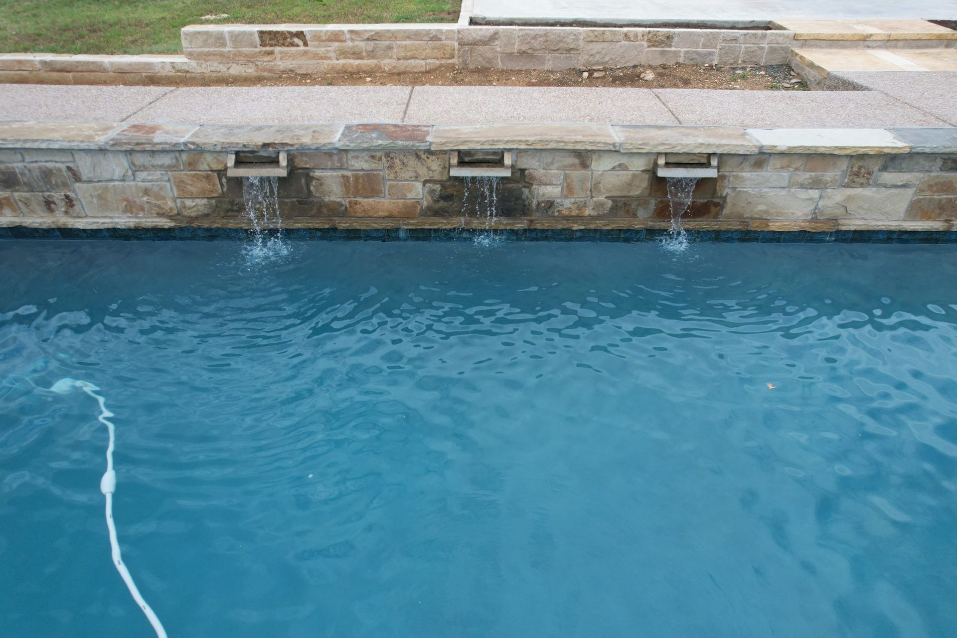 Blue swimming pool beside a stone deck with a white hose floating in the water