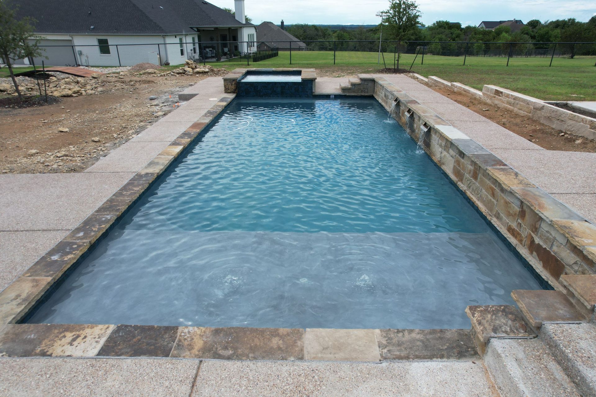 Rectangular backyard swimming pool with blue water and stone coping, viewed from the shallow end.
