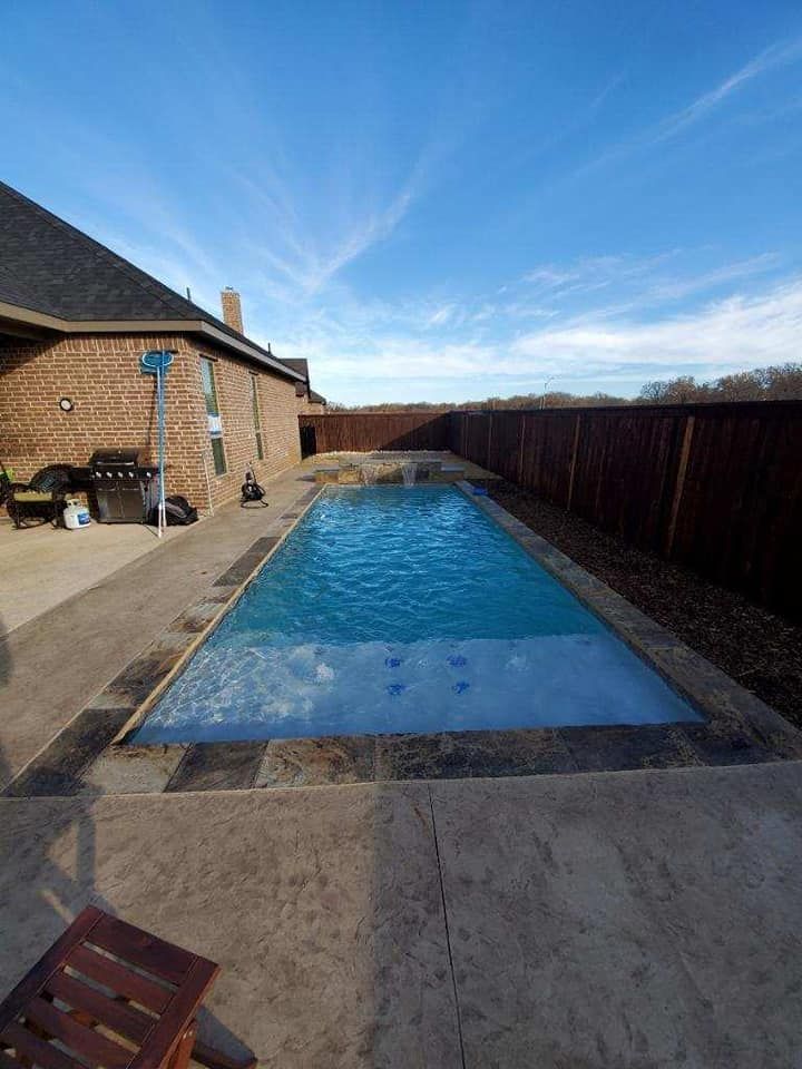 Backyard swimming pool beside a brick house and wooden fence under a blue sky