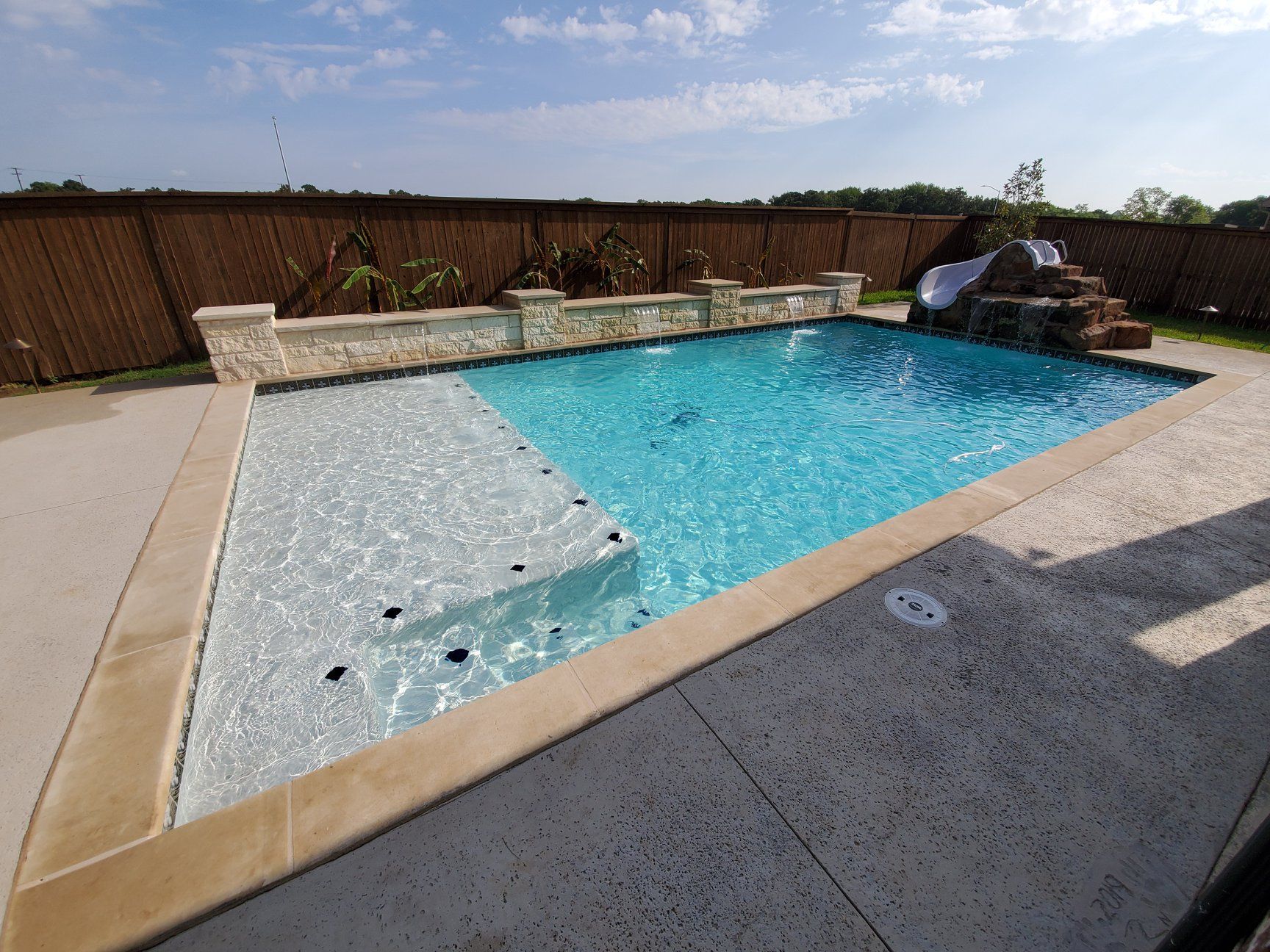 Backyard swimming pool with blue water, stone deck, and a wooden privacy fence