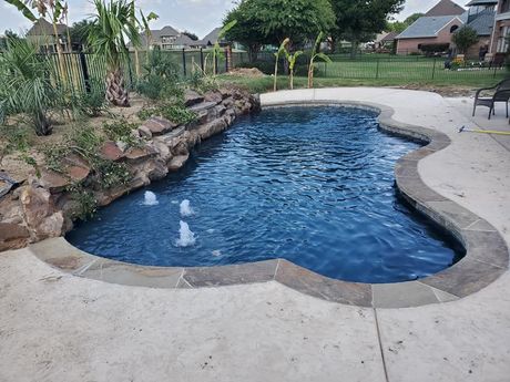 Backyard swimming pool with blue water, stone edging, and a concrete patio