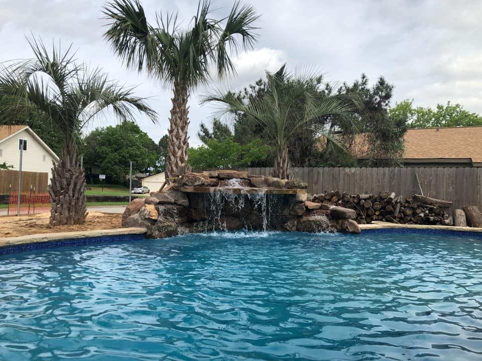 Backyard pool with a rock waterfall, palm trees, and a clear blue sky