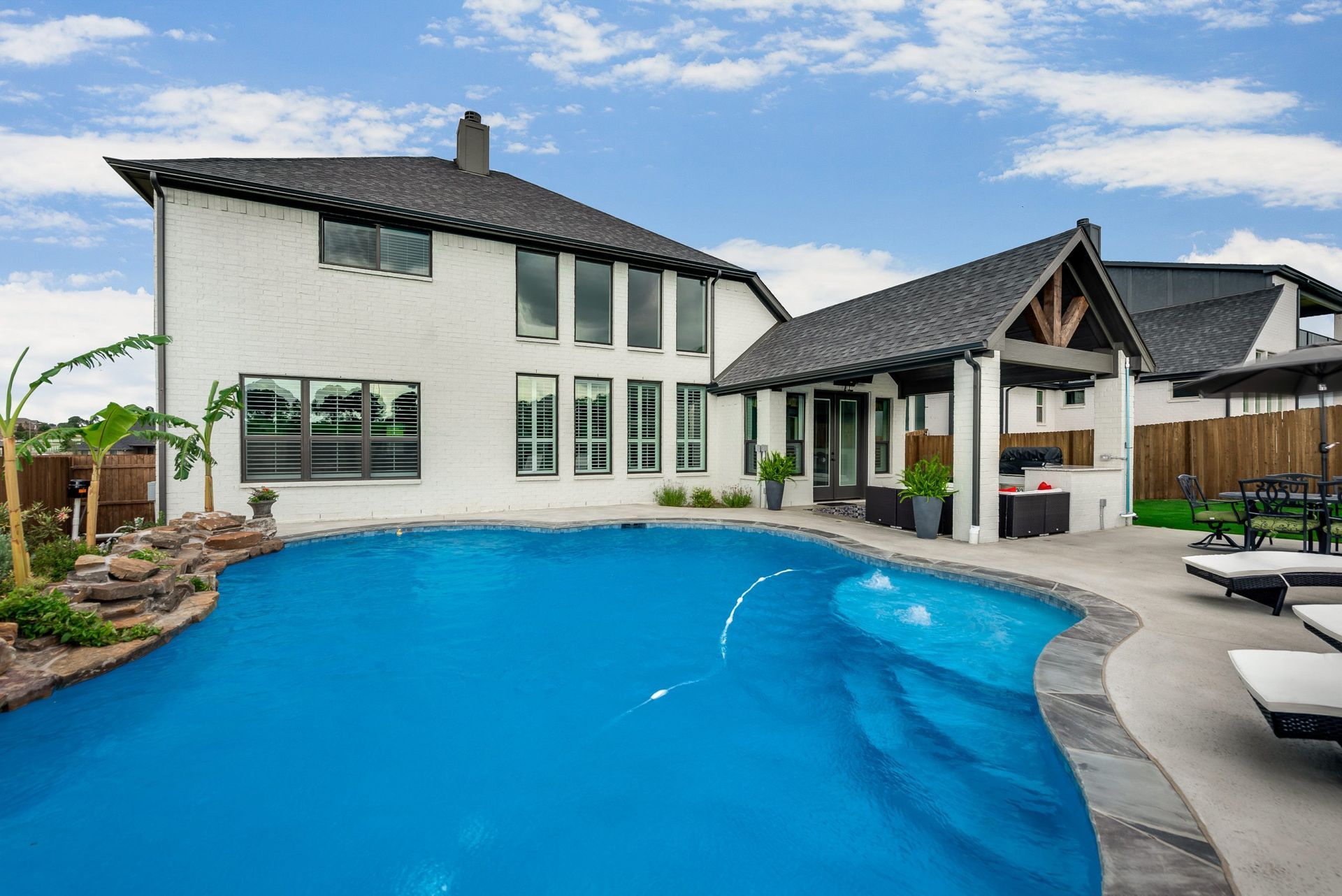 Modern two-story house with a curved blue swimming pool and covered patio in a backyard setting