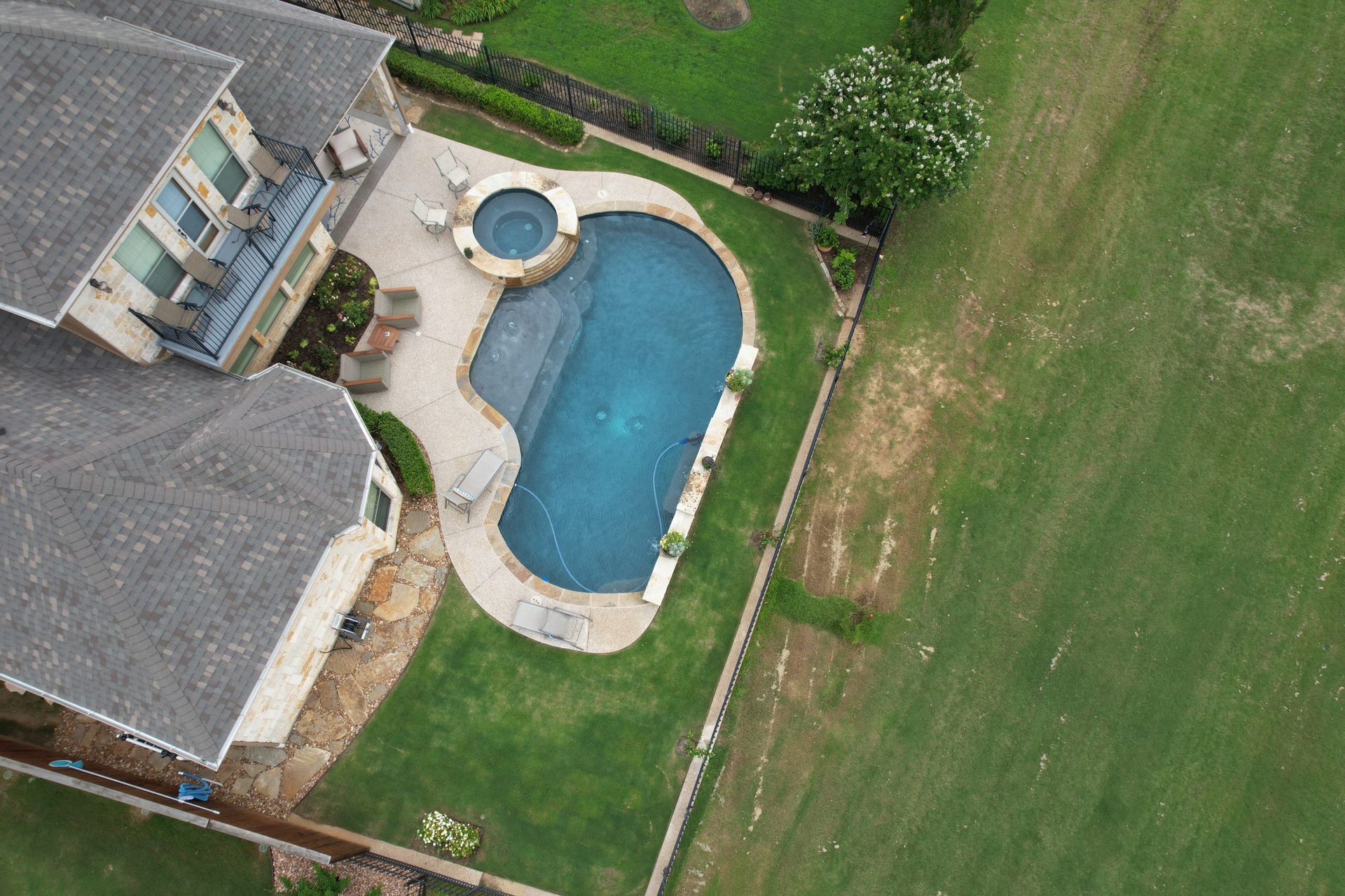 Aerial view of a backyard with a blue swimming pool beside a house and green lawn.
