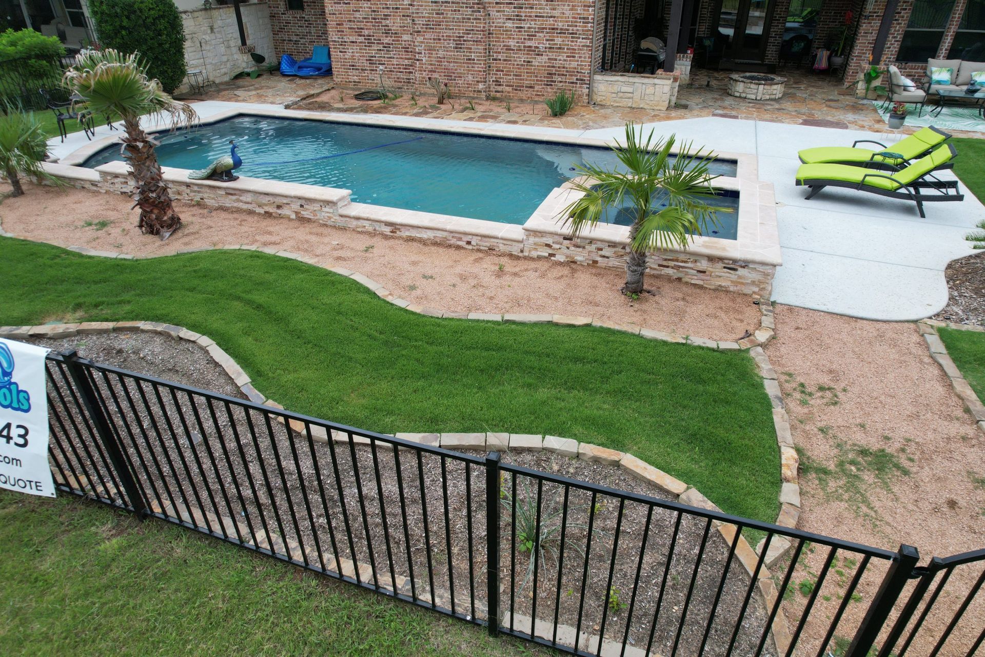 Apartment pool and patio with turquoise water, green lawn, loungers, and black fence view