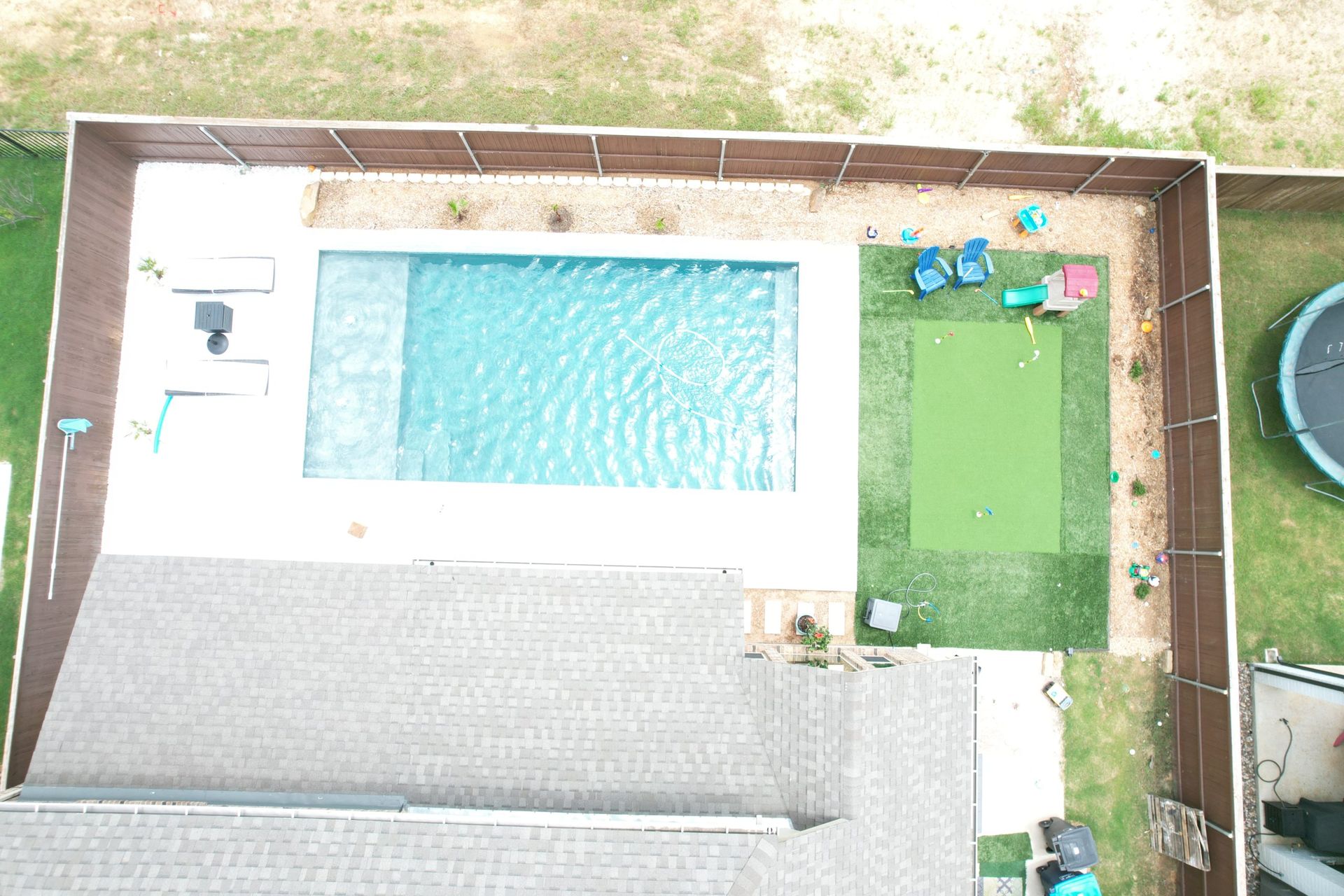 Overhead view of a backyard with a swimming pool, patio, and green lawn area