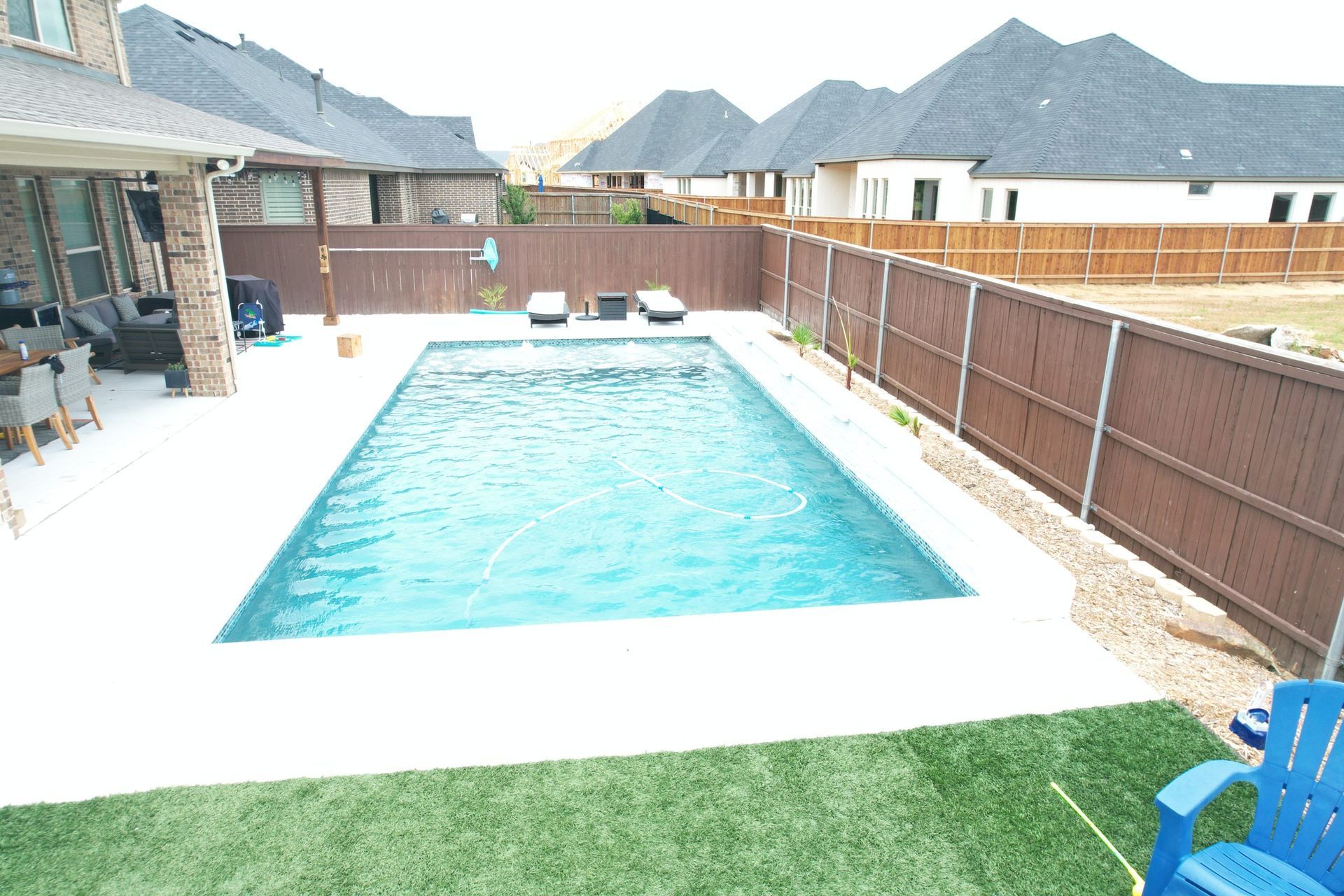 Backyard swimming pool with turquoise water, wooden fence, patio chairs, and mountains in the background