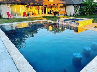 Backyard pool with clear blue water, stone deck, and a lit patio at sunset