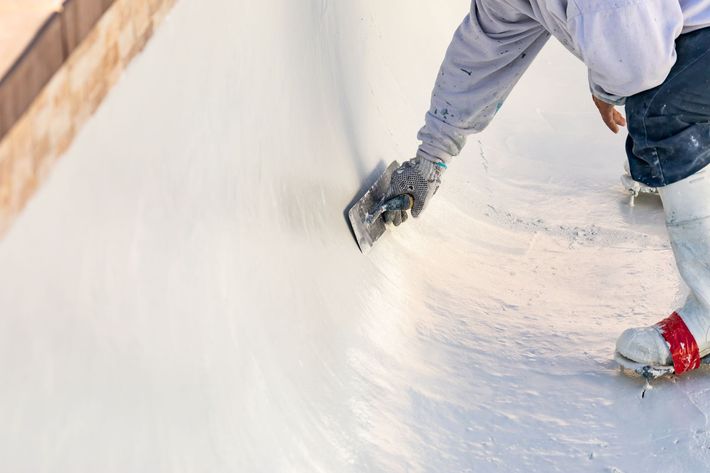 Person smoothing white plaster on a curved wall with a trowel, wearing work gloves and jeans