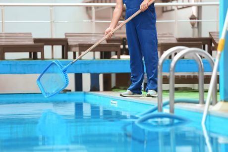 Person skimming debris from a blue swimming pool with a net