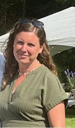 Een vrouw lacht buiten in een groene jurk, met een zonnebril op haar hoofd en een witte tent op de achtergrond.