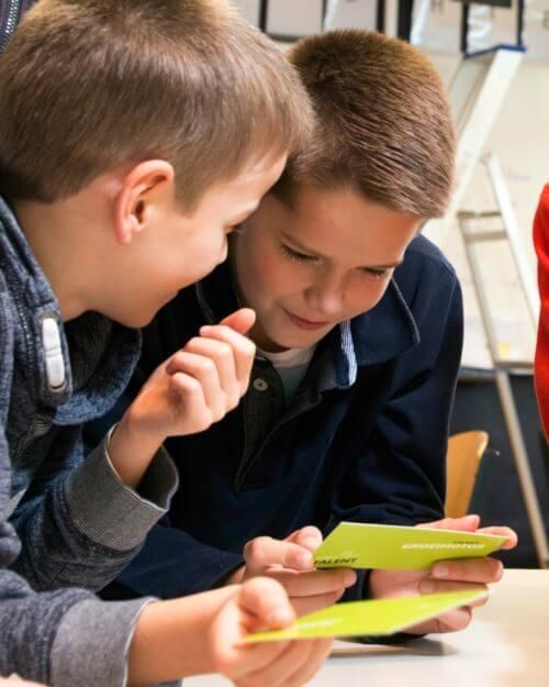 Twee kinderen buigen zich over een tablet en kijken geconcentreerd naar het scherm in een klaslokaal.