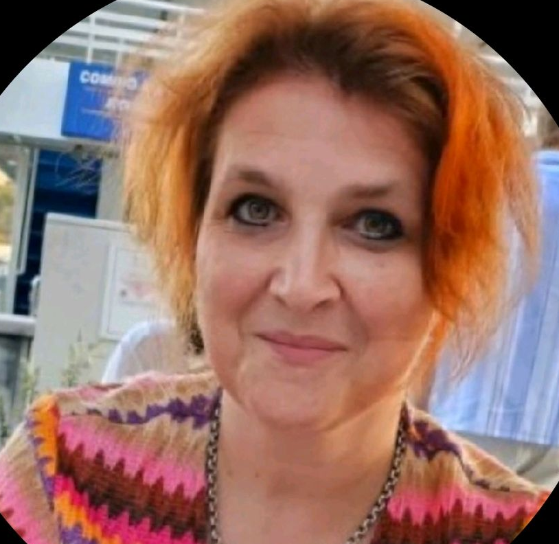Close-up portret van een lachende vrouw met kort oranje haar en een kleurrijke top met zigzagpatroon.