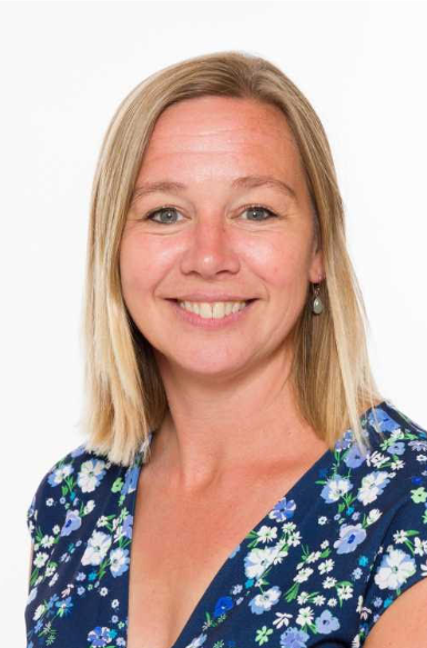 Lachende vrouw met blond haar, gekleed in een blauwe top met bloemenprint, tegen een witte achtergrond.