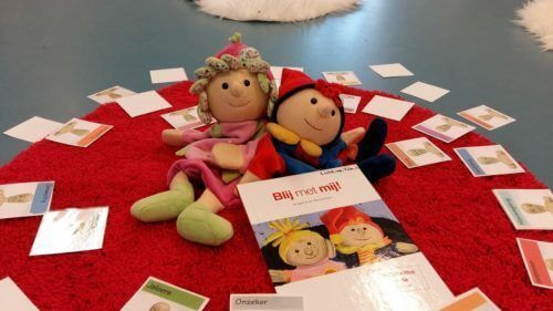 Twee poppen op een rode presentatiemat, omringd door kleine kaartjes en papiertjes op een blauwe ondergrond.