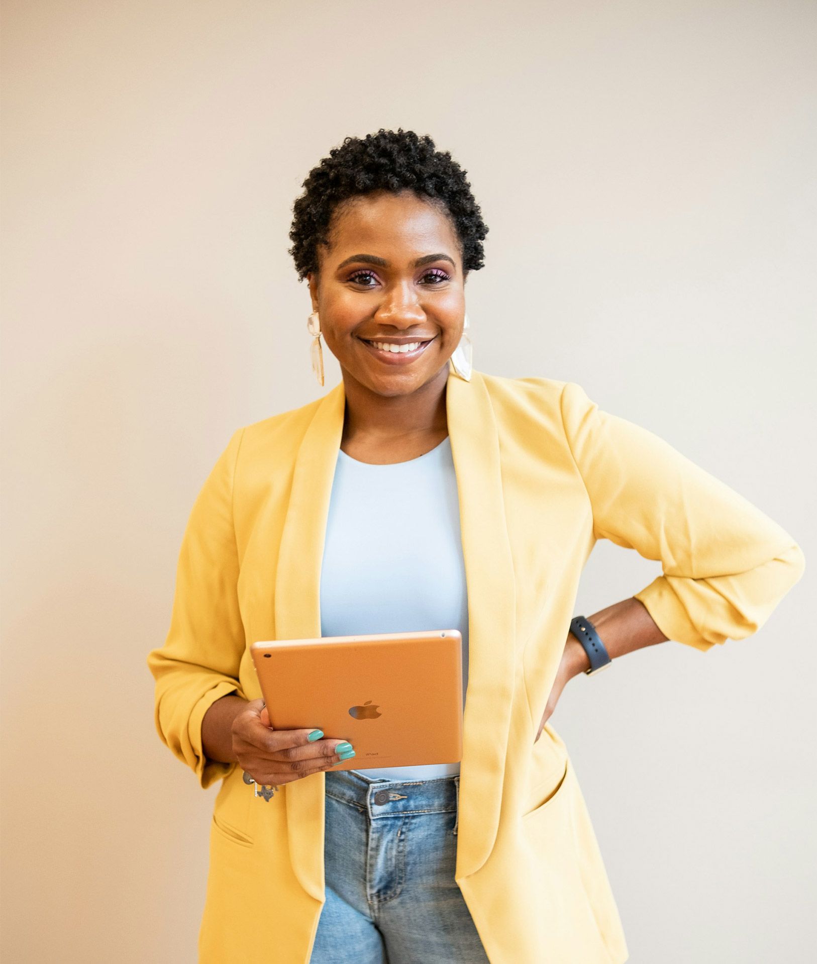 Woman with large afro smiles, holding pen and notebook in terracotta-colored outfit.