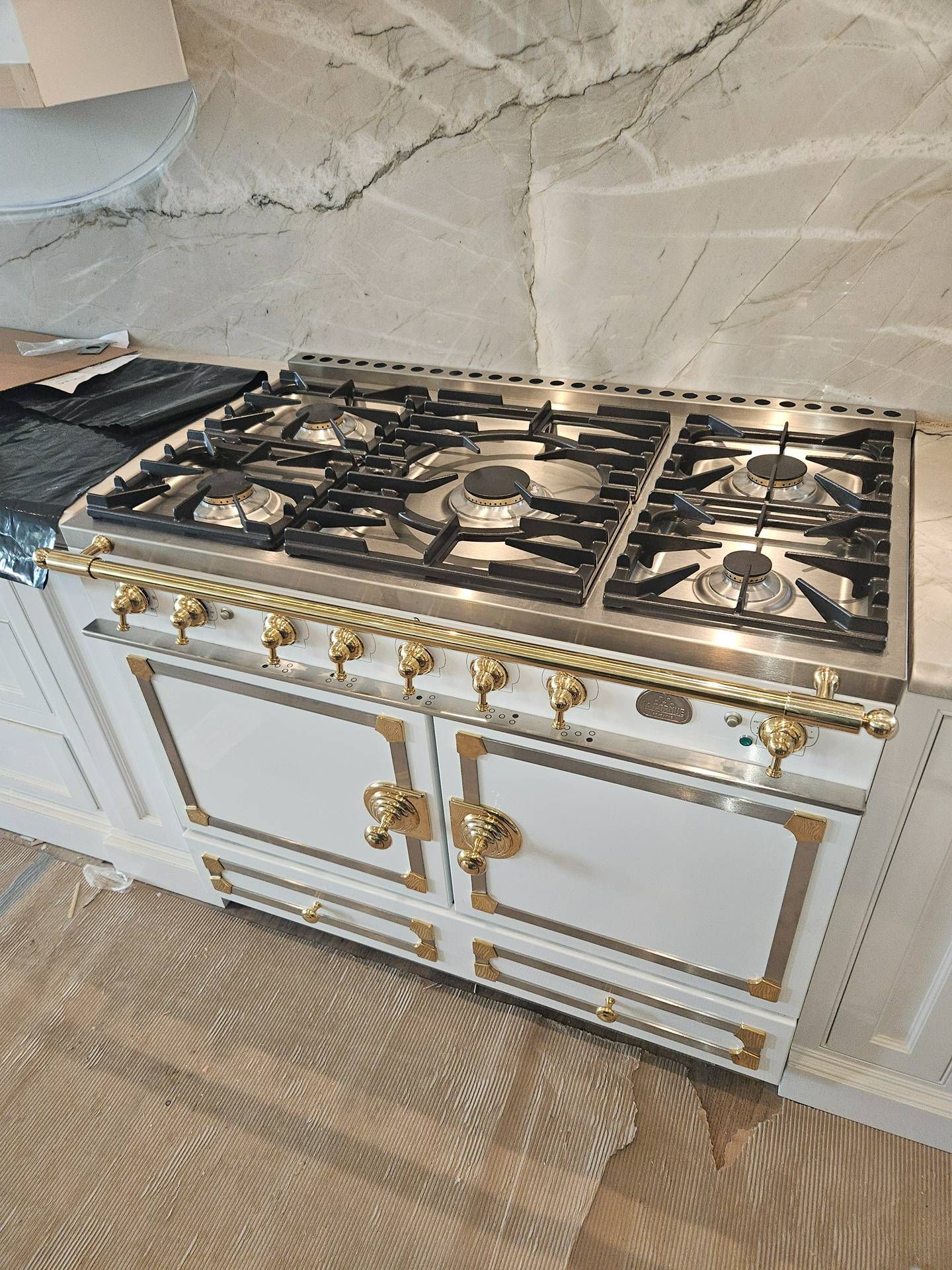 White ornate kitchen stove with black grates and gold trim against a marble backsplash
