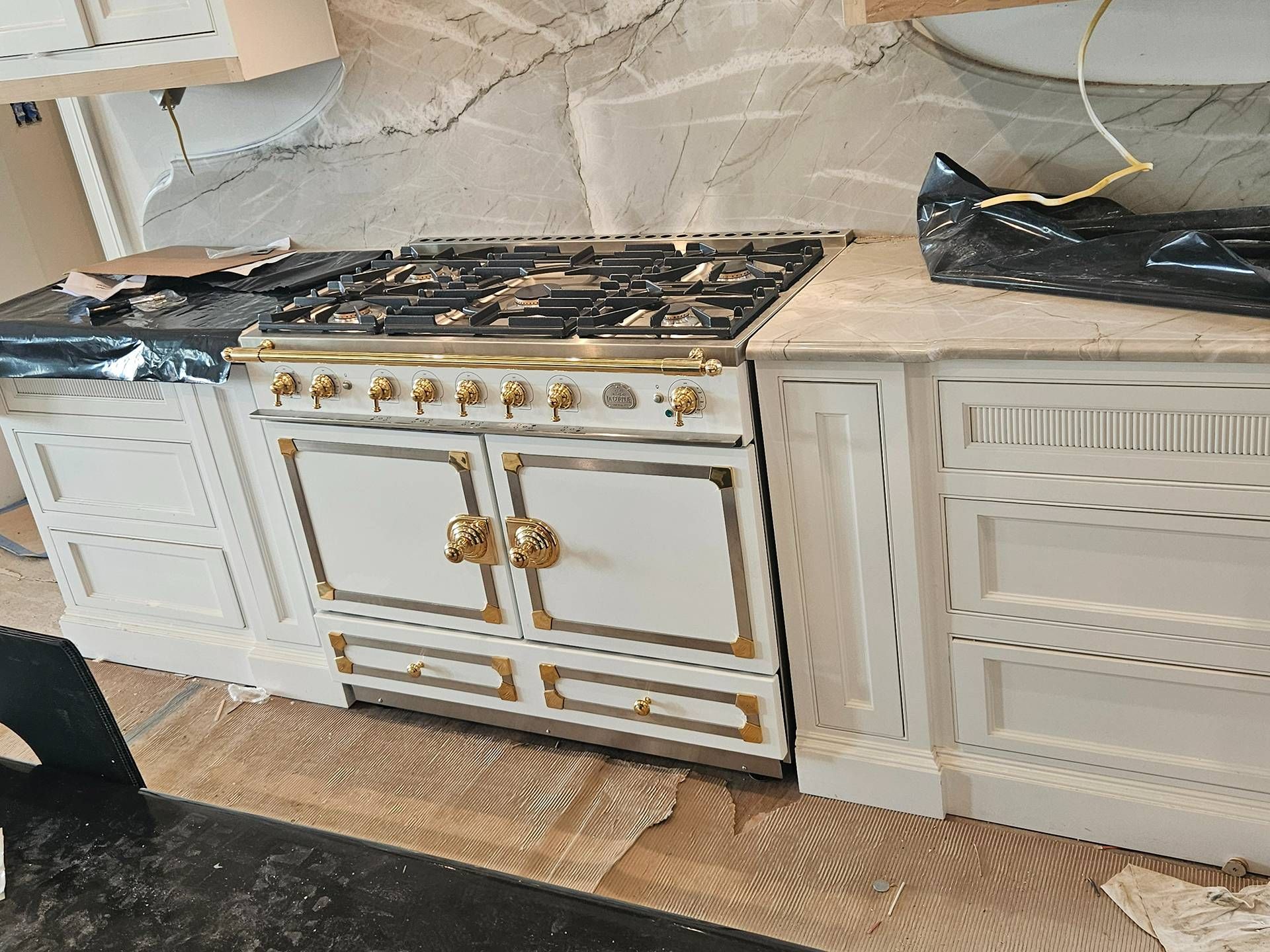 White and gold kitchen stove with ornate trim between white cabinets in a partially finished kitchen