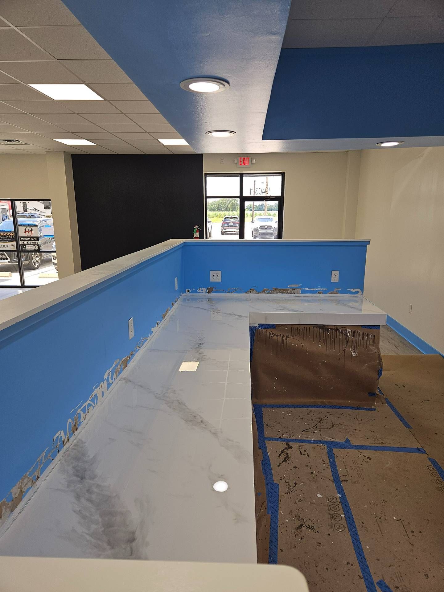Empty room with blue half-walls, tiled floor, ceiling lights, and a glass door at the far end