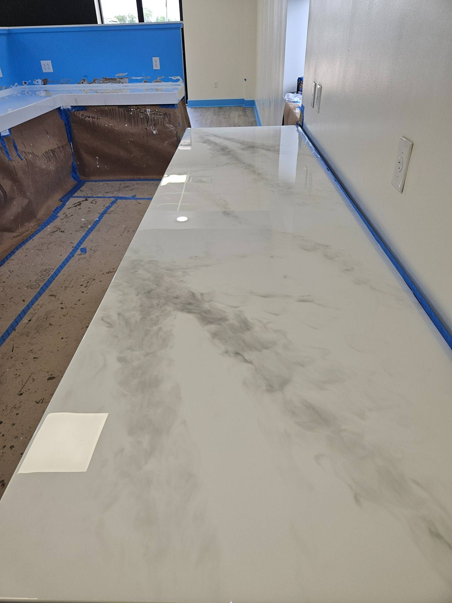 Kitchen countertop with white marble-look surface, blue painter’s tape, and plastic-covered cabinets under renovation