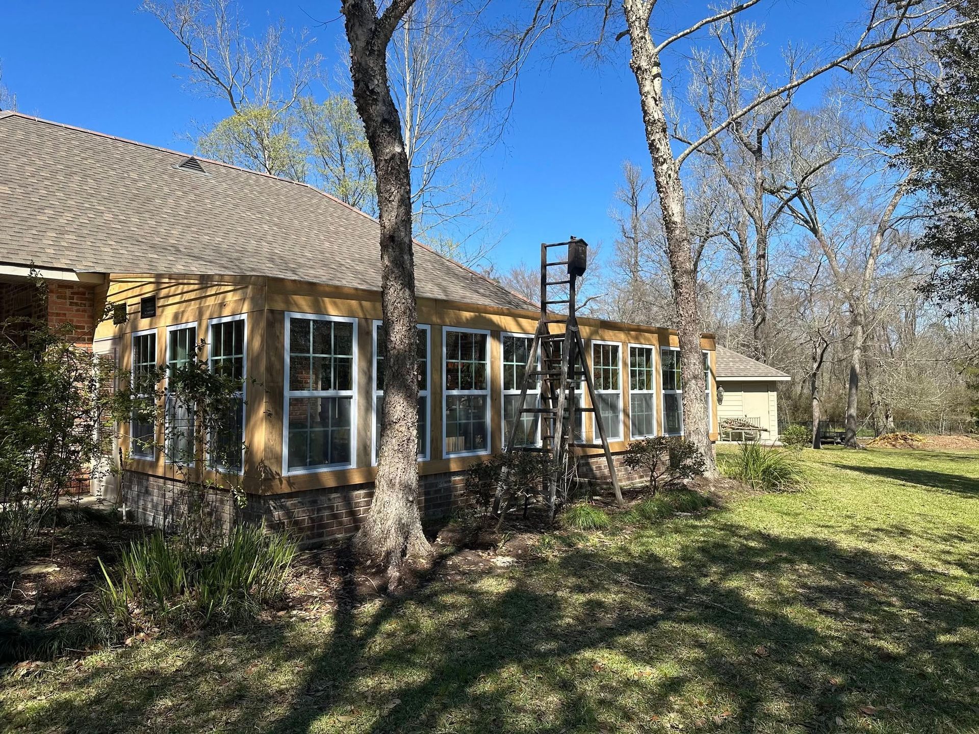 Brick house with large windows beside leafless trees under a bright blue sky