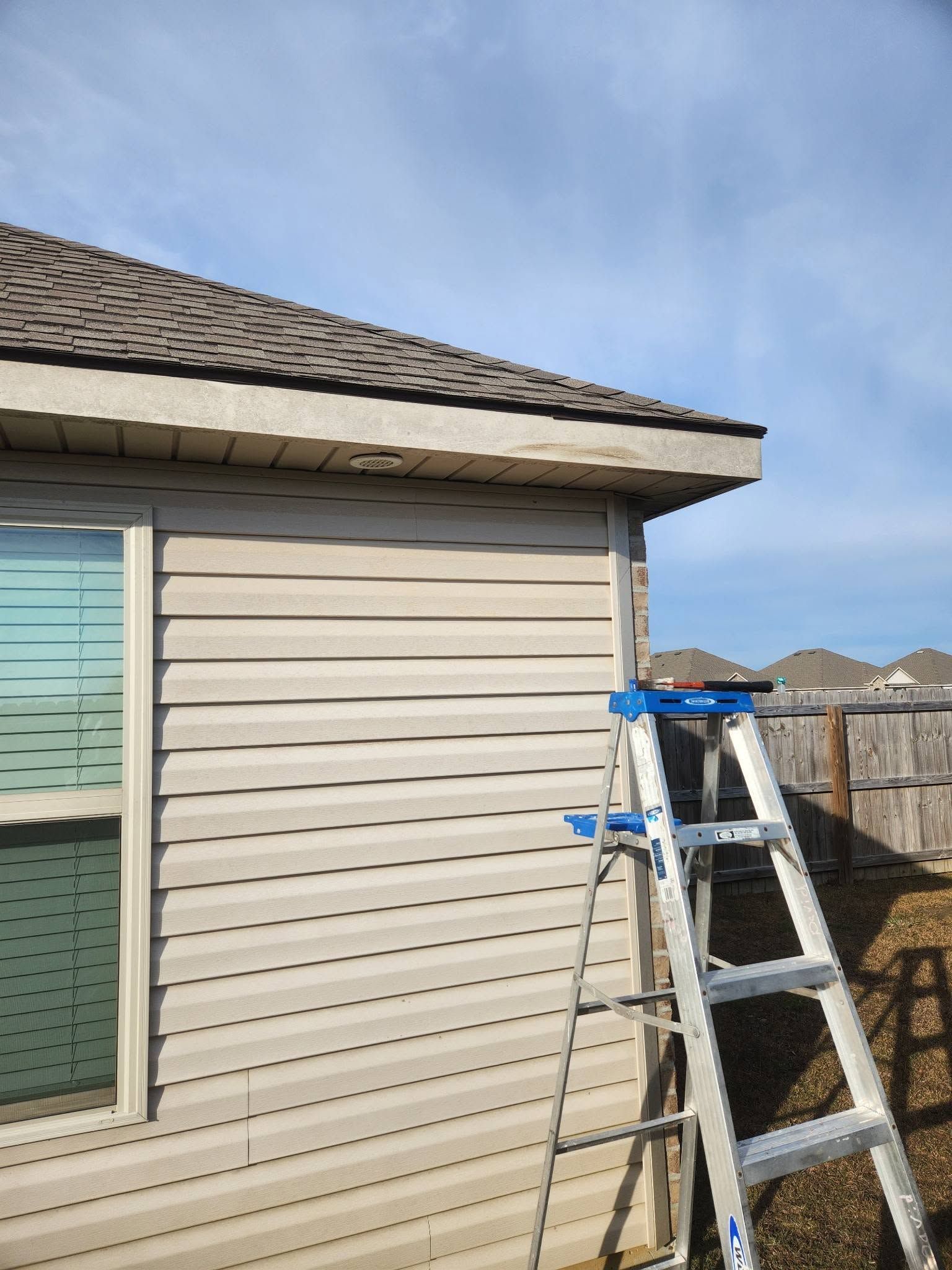 Aluminum ladder leaning against beige house siding under a clear blue sky