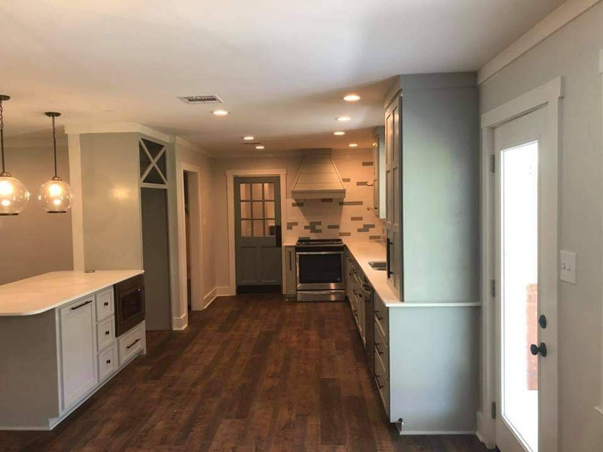 Bright modern kitchen with dark wood floors, white cabinets, gray walls, and a door to outside.