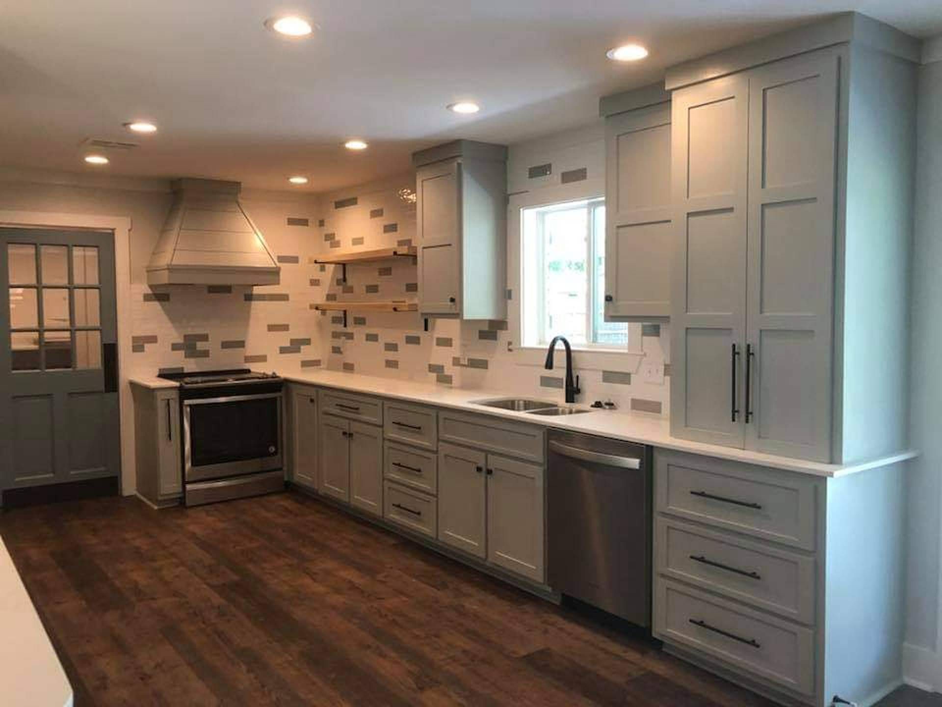 Modern kitchen with gray cabinets, stainless appliances, white tile backsplash, and dark wood floors