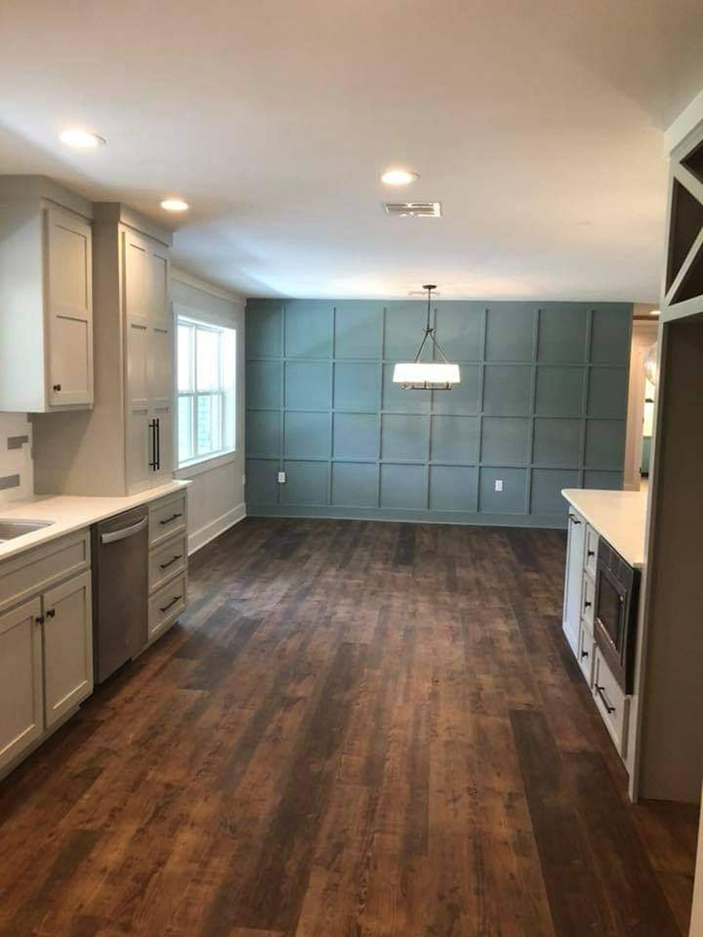 Empty modern kitchen with dark wood floors, white cabinets, and teal accent wall in a bright open room