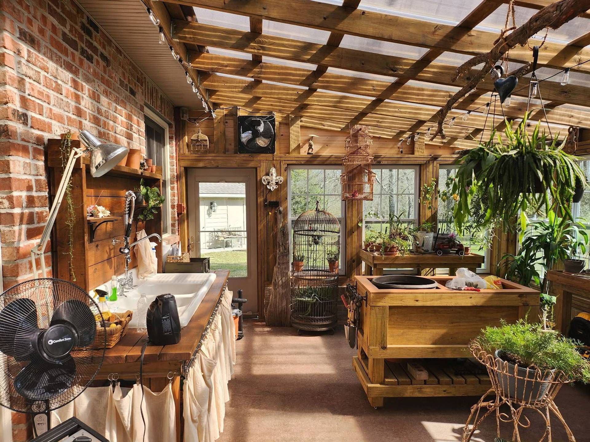 Sunlit rustic greenhouse with brick walls, wooden tables, hanging plants, and potted greenery