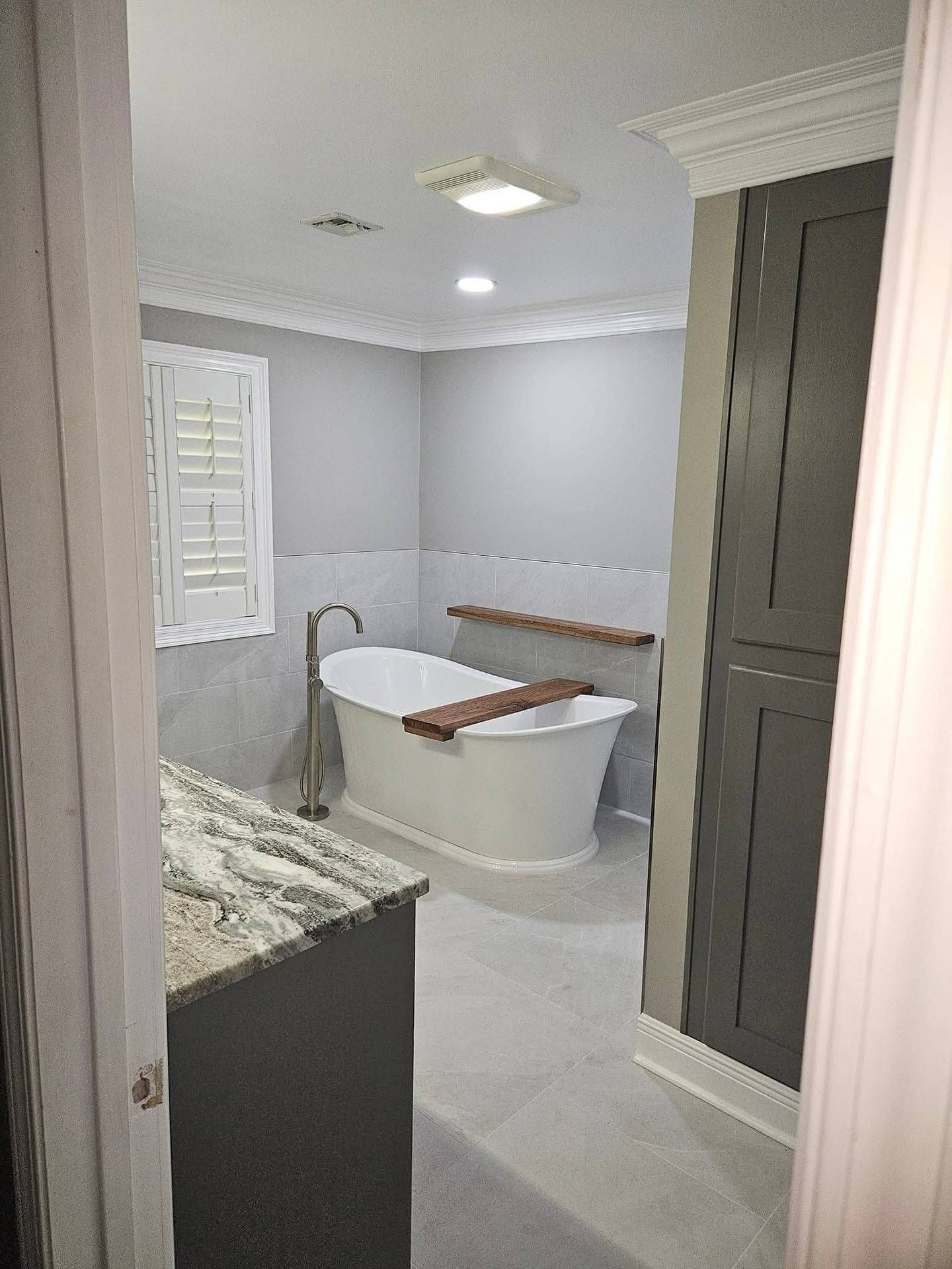 Small gray bathroom with a freestanding tub, white towel, window, and dark vanity cabinet.