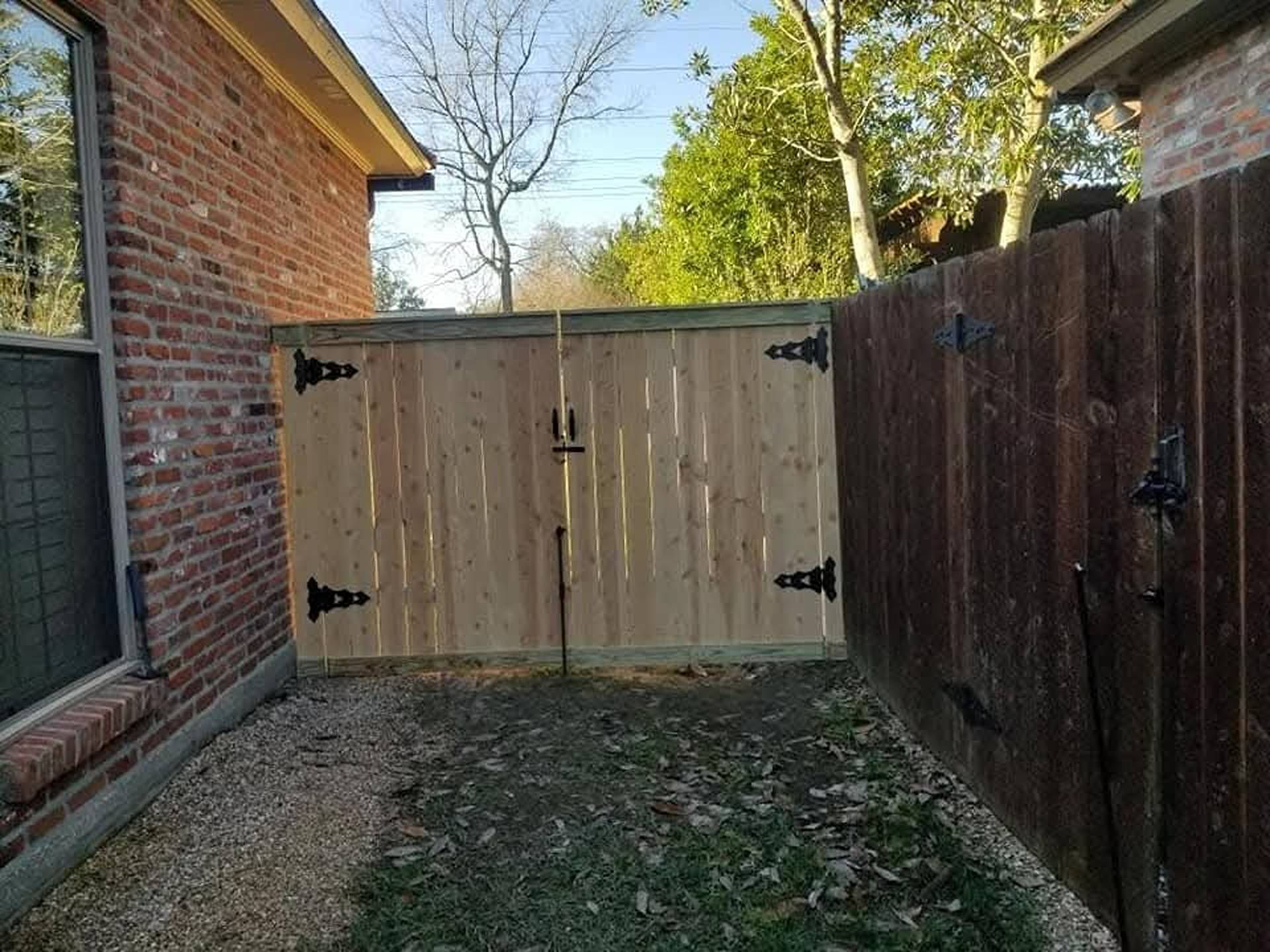 Backyard wooden gate between a brick house and a dark fence with leafless trees overhead