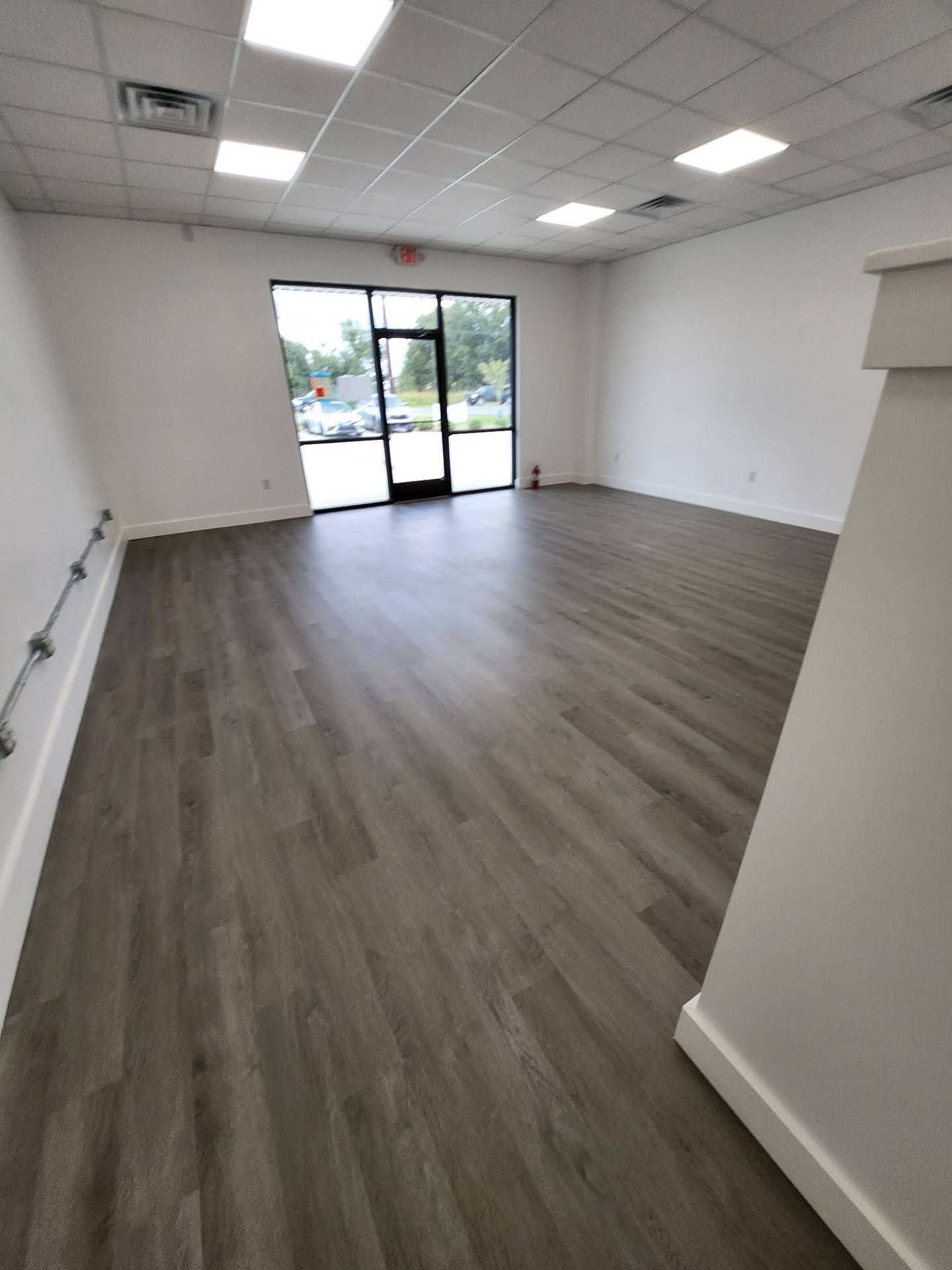 Empty office space with gray wood flooring, white walls, and glass entry doors.