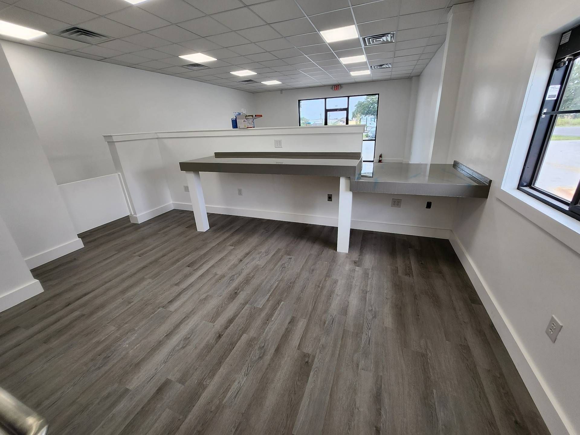 Empty modern office room with white walls, wood-look floor, and built-in counters by windows.