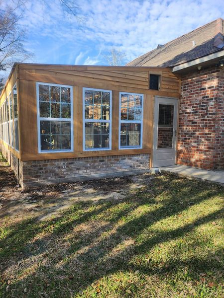 Small brick and wood house addition with large windows and a side door beside a grassy yard.