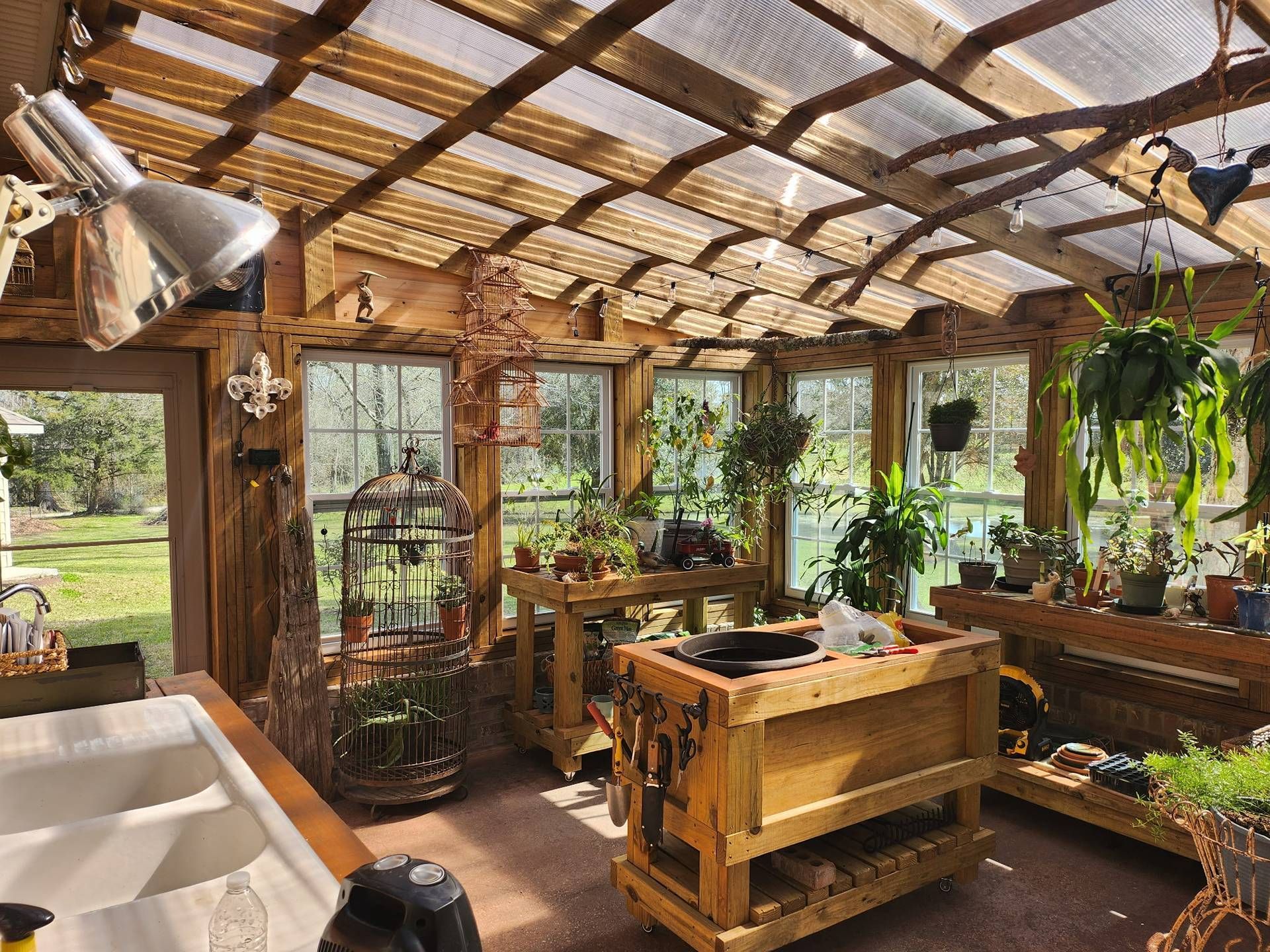 Bright sunroom greenhouse with wooden tables, potted plants, and large windows filled with greenery