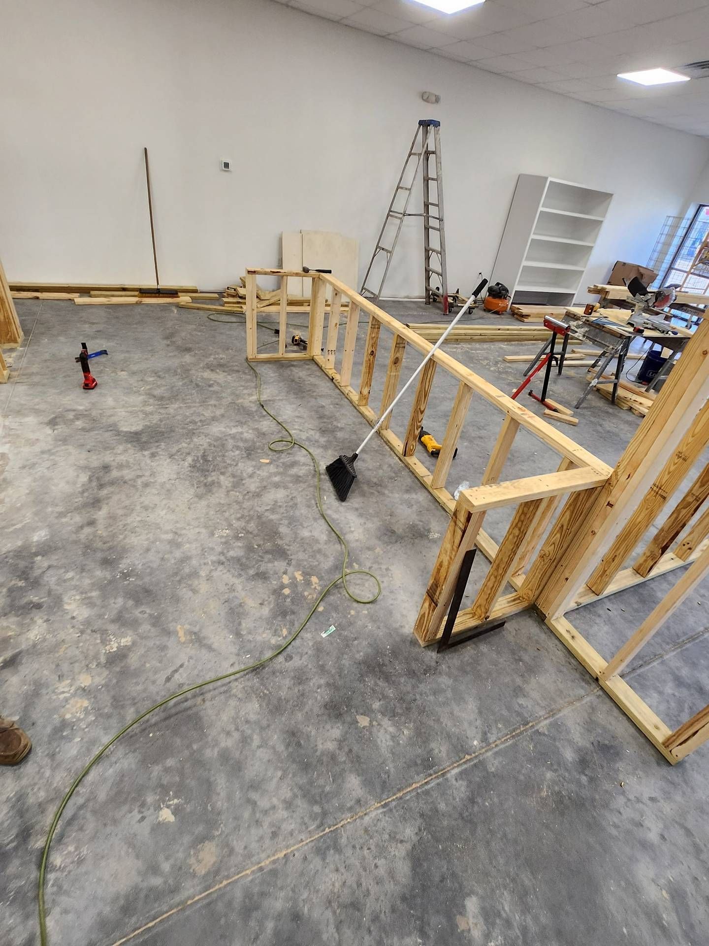 Wood-framed construction barrier in a warehouse-like room with concrete floor, ladder, and tools.