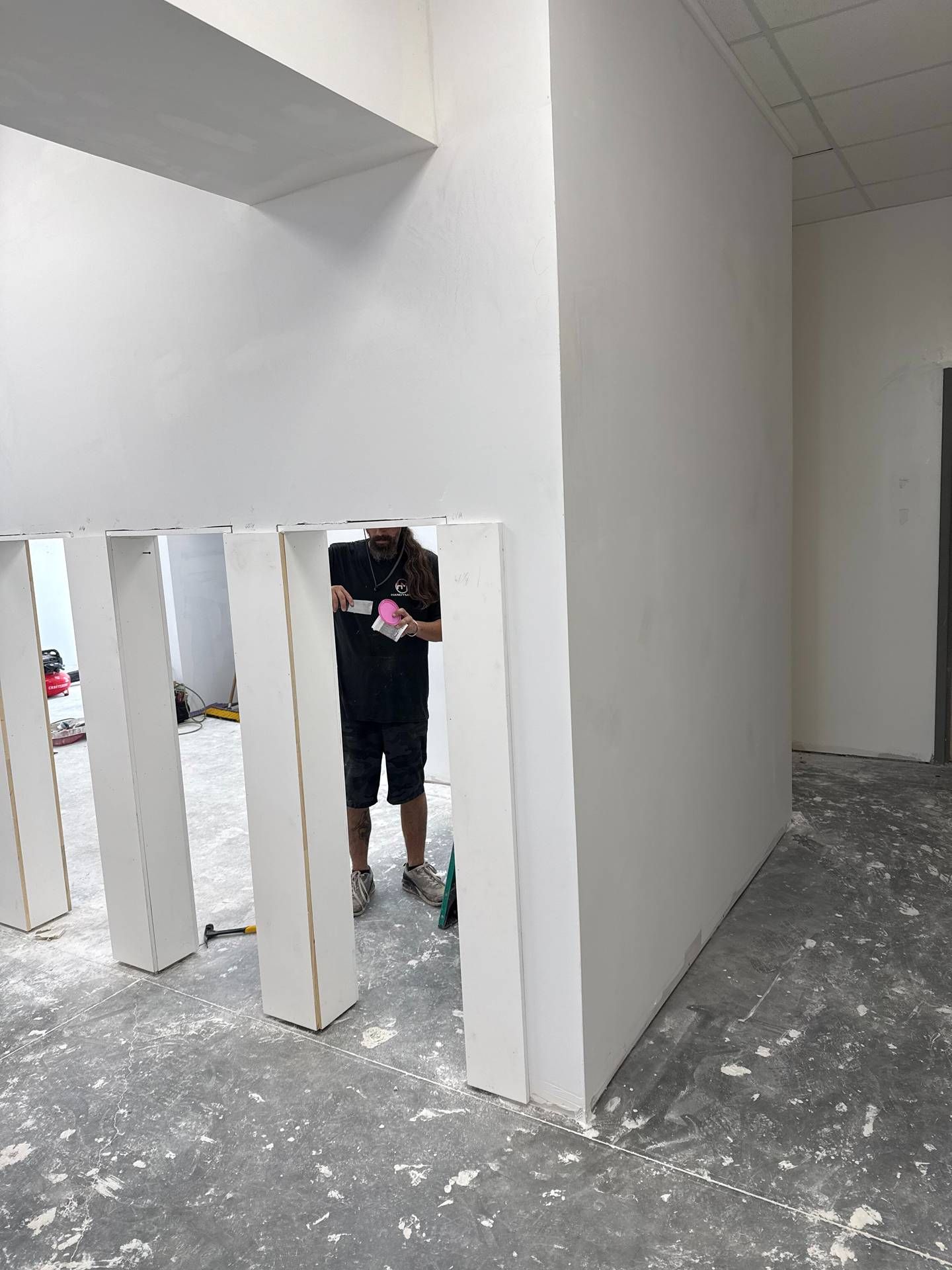 Person standing behind white vertical slats in an unfinished hallway with gray concrete floor.