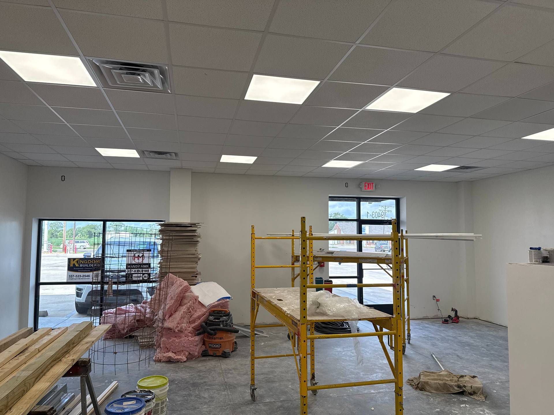 Empty commercial space under renovation with yellow scaffolding, exposed ceiling, and construction materials.