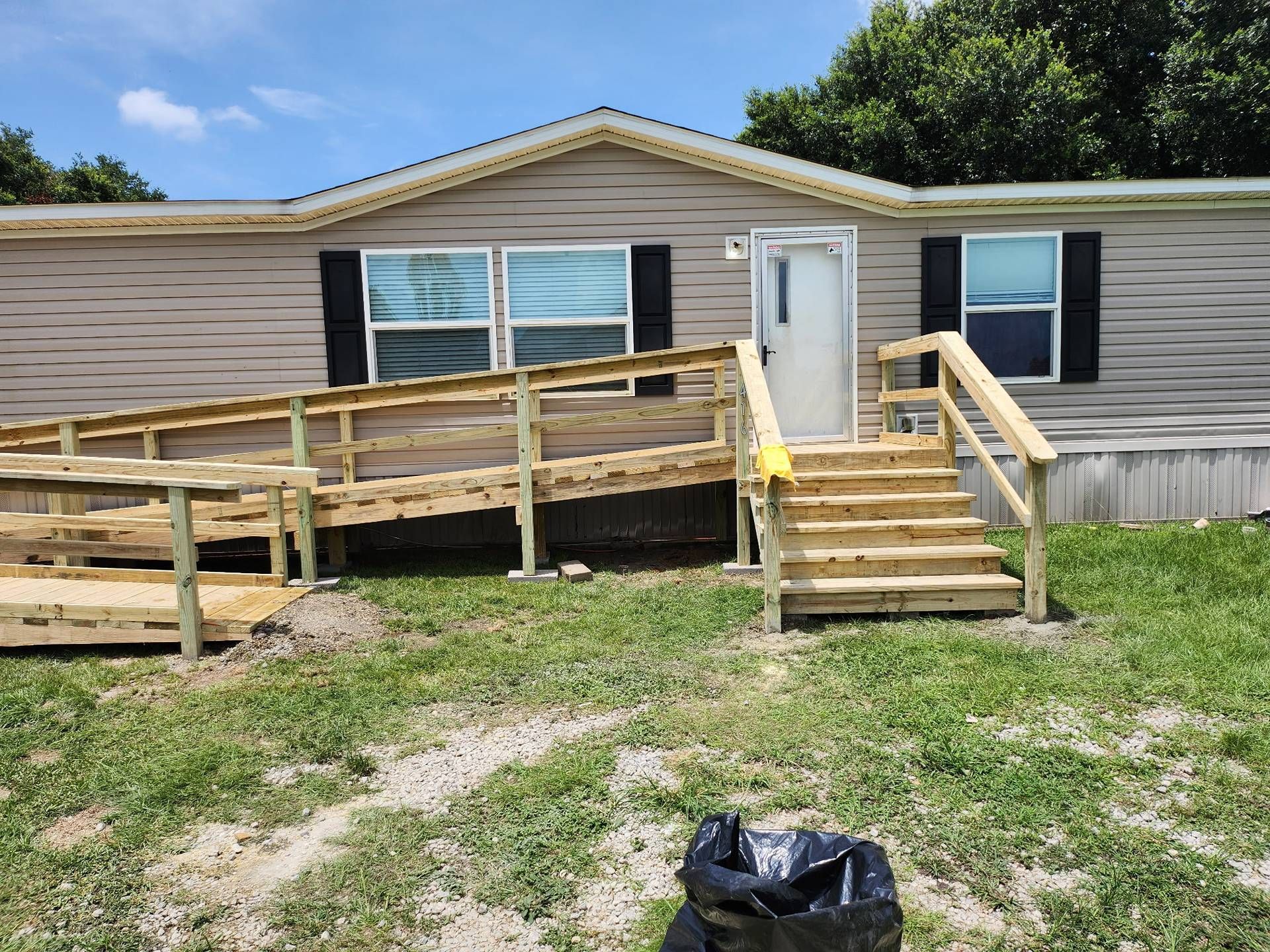 Front of a beige house with a wooden wheelchair ramp and steps leading to the white door.