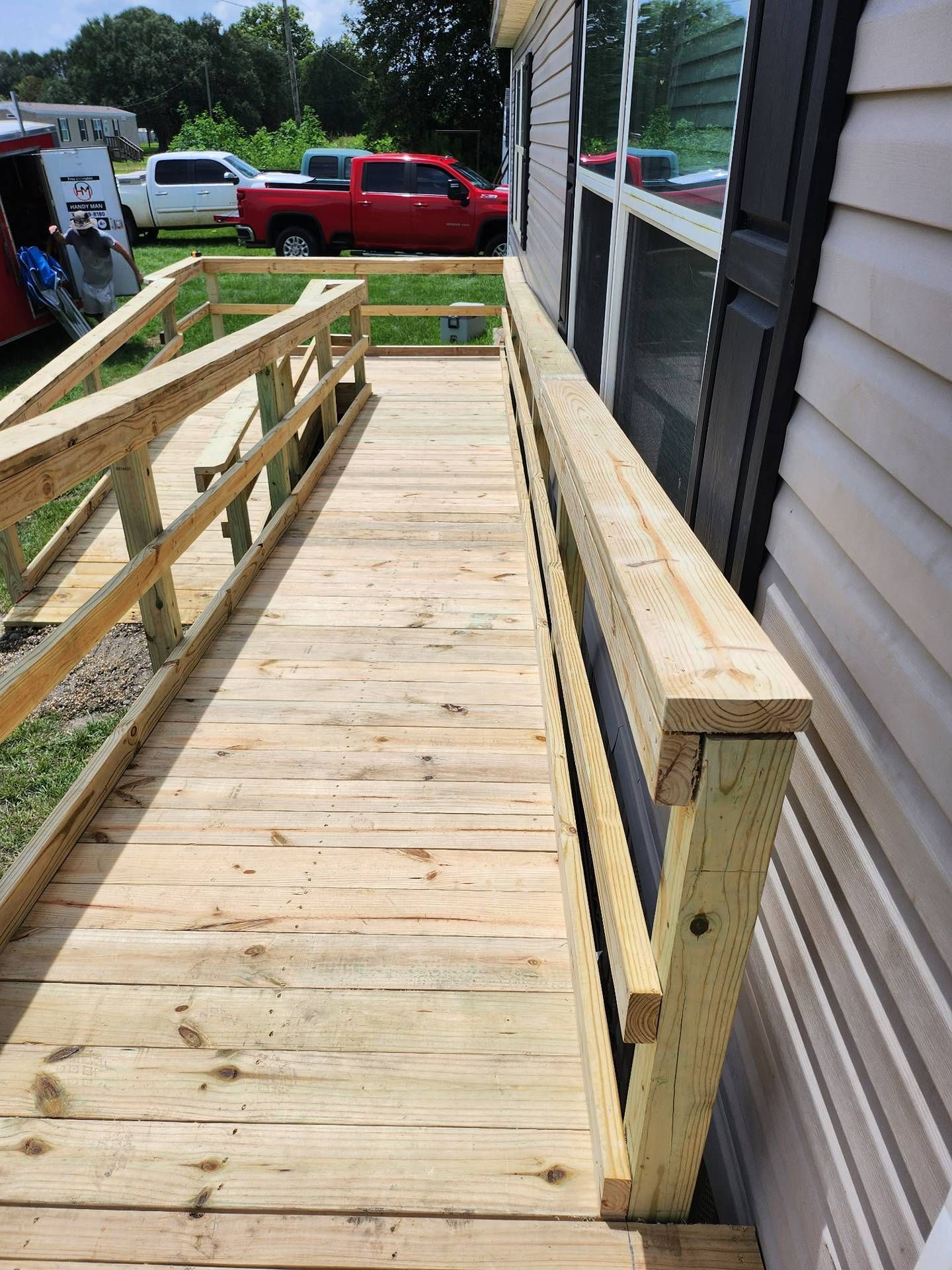 Wooden ramp under construction beside a house, with railings and a red pickup truck in the background.
