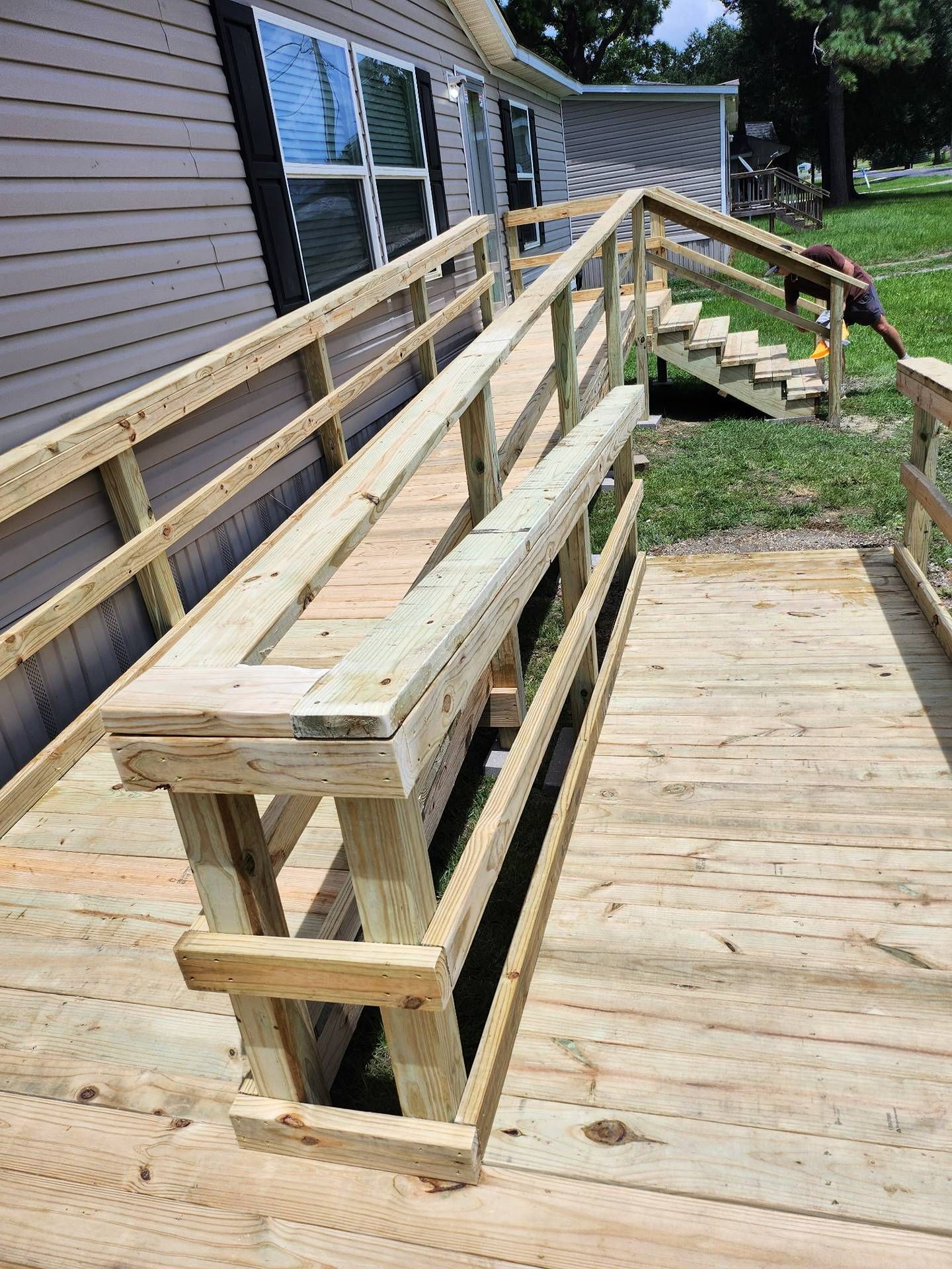 Wooden accessibility ramp with handrails beside a house, leading down to a grassy yard.