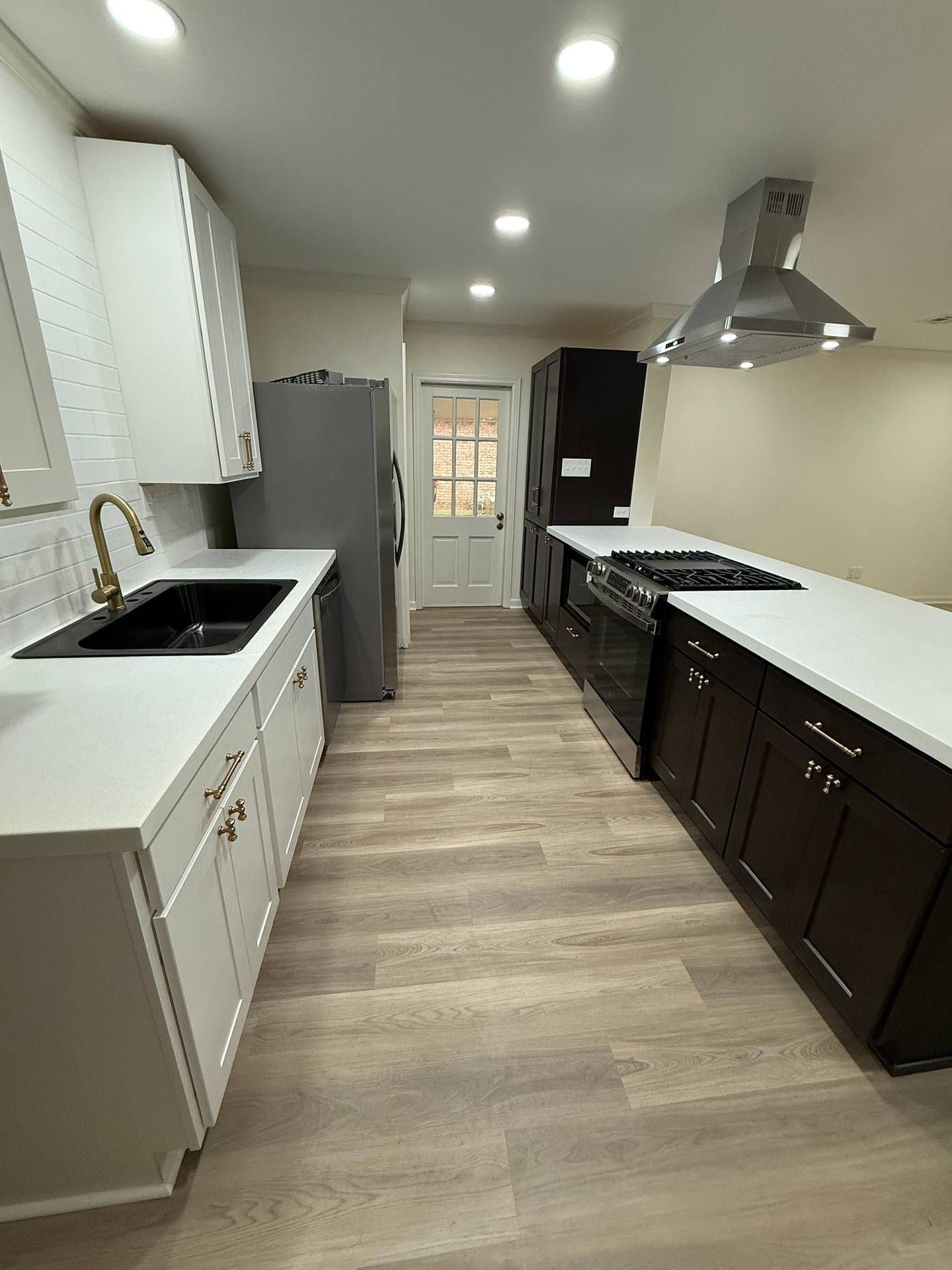 Long galley kitchen with white cabinets, dark lower cabinets, stainless hood, and wood-look flooring