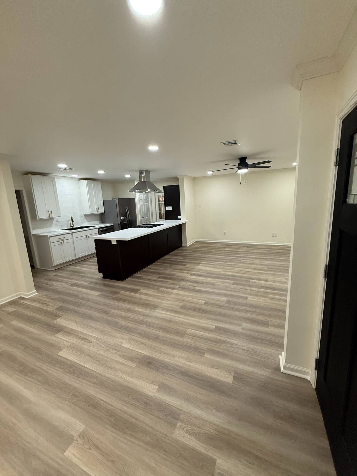 Empty modern kitchen and open living area with wood floors, white walls, and ceiling lights