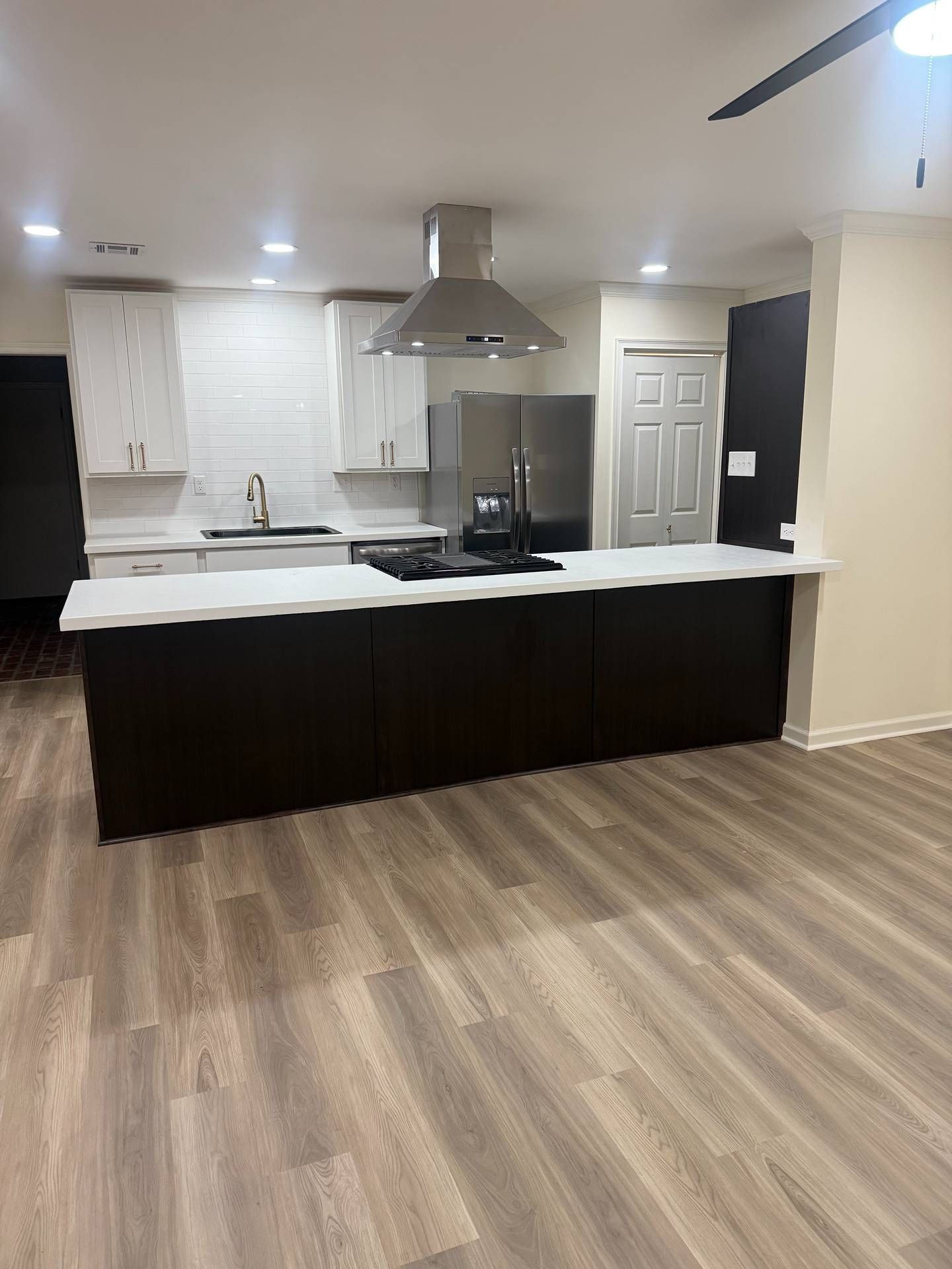 Modern kitchen with dark cabinets, white countertops, island, stainless range hood, and wood-look flooring